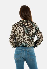 Doorzichtige, multi-kleurige dierenprint blouse met lange mouwen, gecombineerd met blauwe denim jeans met achterzakken en beige stiksels.