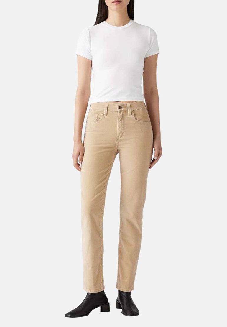 Jean en coton beige avec cinq poches, une fermeture avant à bouton et à glissière, et une coupe droite. Assorti à un t-shirt blanc ajusté et des bottines noires.