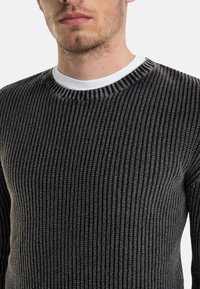 Maglione a coste ribattuto nero e grigio con collo bianco rotondo e maniche lunghe. Superficie testurizzata con linee verticali, design aderente.