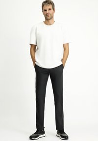Witte korte mouwen T-shirt gecombineerd met zwarte slim-fit broek en zwarte sportschoenen, tegen een effen achtergrond.