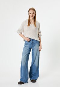 Maglione lavorato a maglia crema con scollo a V, abbinato a jeans in denim azzurro chiaro a gamba ampia. L'outfit presenta una vestibilità comoda e una texture a coste.