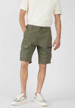 Mand iført olivengrønne cargoshorts med flere lommer, en hvid kortærmet skjorte og hvide sneakers med grå detaljer.