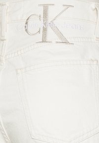 Bílé džíny z denimu s jemnou texturou. Obsahují zadní kapsu a vyšitý logo "CK" s textem "calvinKleinJeans" ve světlé nitě.