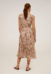 Blumenkleid in Midi-Länge mit einem plissierten Design, in sanften Rosa- und Grüntönen. Das Kleid hat kurze Ärmel und eine taillierte Taille, kombiniert mit flachen Sandalen.