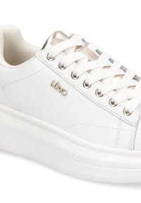 Zapatilla blanca de cuero con cordones blancos, logo metálico dorado en el costado y detalle dorado a juego en el collar de la lengüeta.