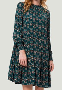 Vestido color aguamarina con estampado floral, mangas largas, escote fruncido y dobladillo de volantes. Hecho de una tela suave con un diseño fluido.