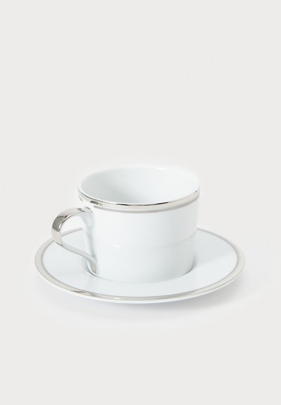 Biely porcelánový kávový šálka so strieborným okrajom, doplnený o zodpovedajúci tanier. Hladká textúra a zaoblený tvar zdôrazňujú jeho elegantný dizajn.