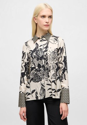 Blusa a fantasia floreale in crema e nero. Caratterizzata da un colletto e maniche lunghe con una stampa geometrica a contrasto sui polsini.