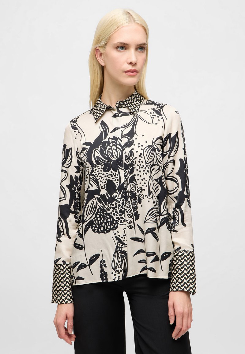 Blusa a fantasia floreale in crema e nero. Caratterizzata da un colletto e maniche lunghe con una stampa geometrica a contrasto sui polsini.