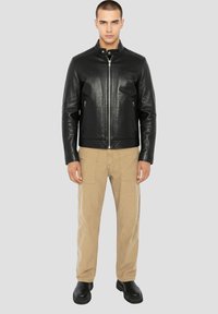 Zwarte leren jas met een hoge kraag, twee zijritszakken, gecombineerd met beige broek en zwarte schoenen. Gladde textuur met een getailleerde pasvorm.