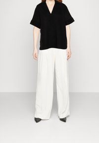 Haut noir à manches courtes avec un col en V et une coupe décontractée, associé à un pantalon blanc à jambes larges et des chaussures noires pointues. Design simple et moderne.