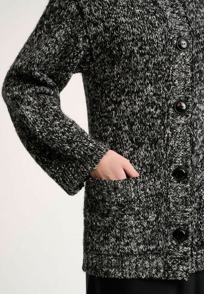Zwart-witte gebreide cardigan met een textuurpatroon, voorzien van een knoopsluiting aan de voorkant, grote knopen en een zijzak.