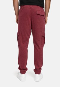 Burgunderfarbene Jogginghosen mit Cargo-Taschen, tailliertem Design, elastischem Bund und gerippten Bündchen. Hergestellt aus weichem, bequemen Baumwollmischgewebe.