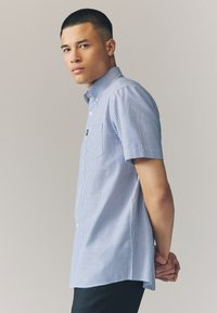 Kortærmet skjorte med knapper, der har et blåt og hvidt stripet mønster, krave og en forlommer; lavet af let stof.