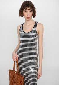 Robe sans manches avec des rayures horizontales noires et argentées, ornée de sequins et d'un col rond. Portée avec un sac tissé texturé de couleur brune.