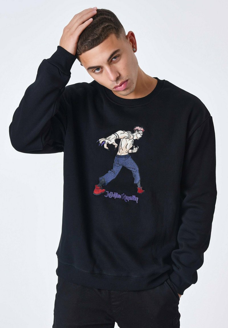 Sweatshirt noir avec un graphique brodé coloré d'un personnage en action, associé à un jean bleu et des chaussures rouges, en tissu texturé, col rond.