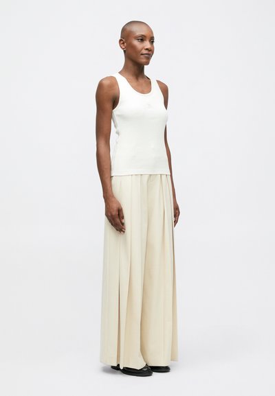 Biele pásikavé tielko v kombinácii s béžovými širokými plisovanými nohavicami a čiernymi topánkami. Hladká látka s priliehavým strihom a minimalistickým dizajnom.