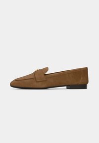 Mocassino in suede marrone con tacco piatto, dotato di linguetta ripiegata e dettagli in metallo dorato. Texture liscia e forma snella.