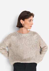 Helle beige gestrickte Pullover mit lockerer Passform, Rundhalsausschnitt und strukturiertem Muster. Lange Ärmel und weiches, glänzendes Material.