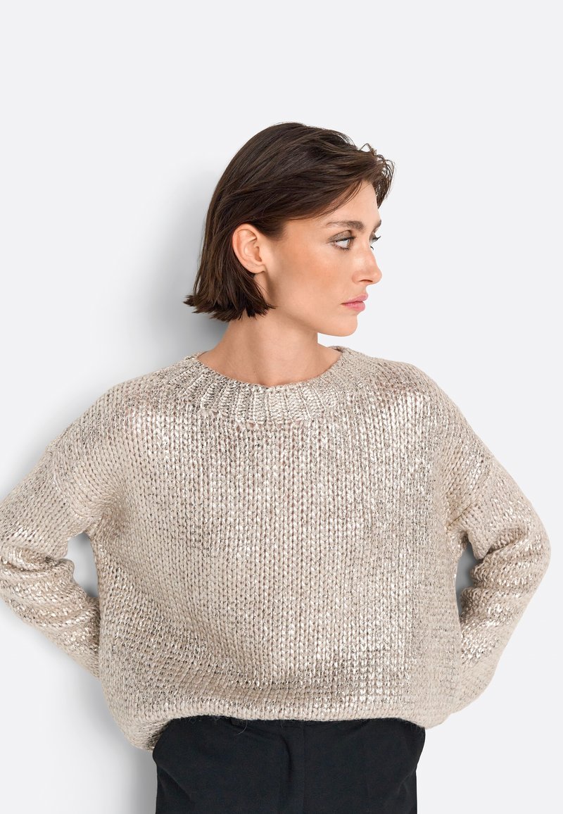 Helle beige gestrickte Pullover mit lockerer Passform, Rundhalsausschnitt und strukturiertem Muster. Lange Ärmel und weiches, glänzendes Material.