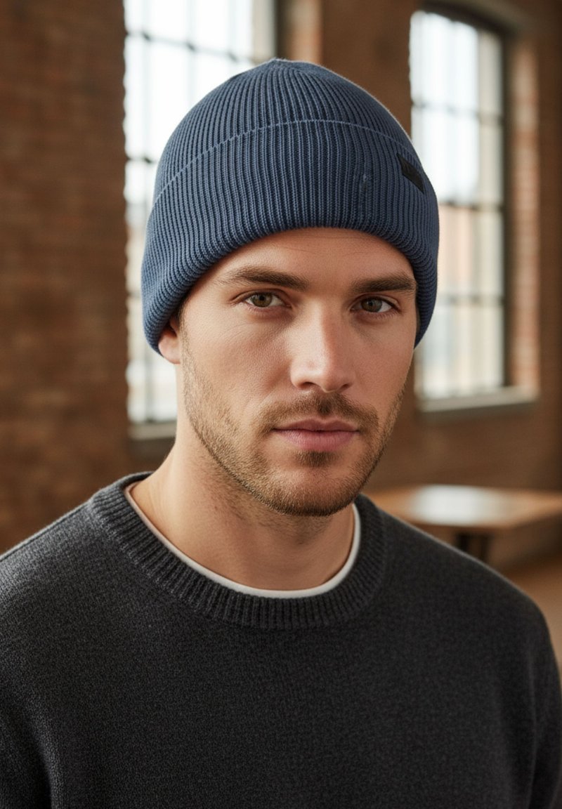 Blue ribbed beanie hat made from knit material, featuring a slight slouch at the top. Worn with a dark gray sweater and white neckline.
