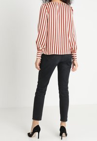 Rød og hvid stribet bluse med puffede ærmer, kombineret med sorte skinny jeans og sorte højhælede sko. Tekstureret stof, afslappet pasform.