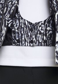 Veste matelassée avec un motif abstrait noir et blanc, dotée de boutons-pression et d'une doublure douce blanche à l'ourlet.