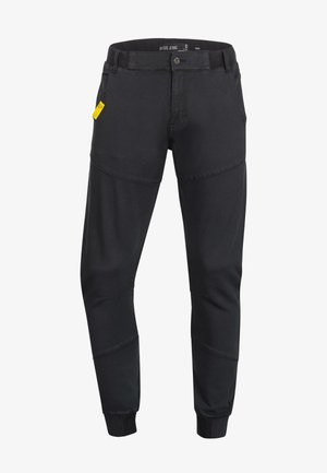 Black tapered jeans with contrasting panel design, elastic cuffs, and a subtle sheen. Features a standard button closure and front pockets.