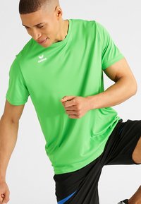 Groene sport T-shirt met korte mouwen, gemaakt van gladde, lichtgewicht stof, met een ronde hals en een logo op de voorkant, gecombineerd met zwarte shorts.