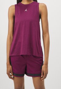 Bordeaux mouwloze sporttop met een ronde hals en een klein wit logo. Gepaarde met bijpassende shorts, ook in bordeaux, met zwarte accenten.