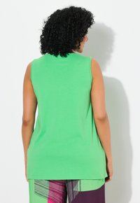 Top verde senza maniche realizzato in cotone, con un taglio dritto e una texture liscia. La parte posteriore è semplice, senza motivi o decorazioni visibili.