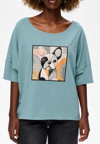 Lichtblauw oversized t-shirt met een kleurrijke illustratie van een Franse bulldog in een vierkante patch. Korte mouwen, zachte textuur.