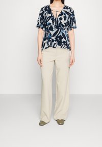 Blusa de patrón azul marino y claro con mangas cortas y flotantes, escote en V y ajuste holgado, combinada con pantalones de pierna ancha color crema.