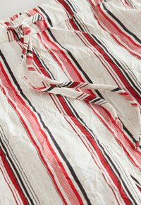 Shorts en tissu léger avec une base blanche, présentant des rayures horizontales rouges et noires, une taille à nouer et une texture froissée.