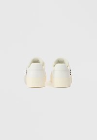 Λευκά δερμάτινα αθλητικά παπούτσια με υφή στην κρεμ σόλα, διακοσμημένα με λογότυπο στο πλάι και λεία φτέρνα. Μινιμαλιστικός σχεδιασμός χωρίς σχέδια.