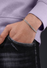 Bracciale d'argento con molteplici accenti circolari indossato su un polso, abbinato a un maglione lavanda e jeans neri strappati.