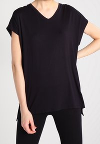 Černý krátký rukáv top s v-výstřihem, měkká tkanina, volný střih a boční rozparky pro snadný pohyb. Jednoduchý, minimalistický design.