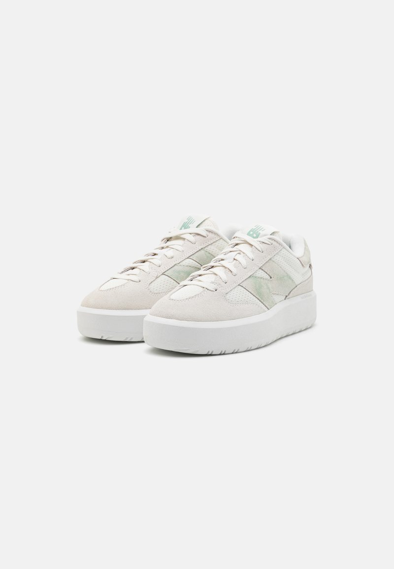 Un paio di sneakers beige scamosciate e in rete a taglio basso con suole spesse bianche e dettagli verde chiaro, vista frontale a tre quarti su sfondo bianco.
