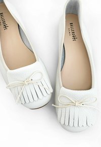 Ballerine in pelle bianca con una finitura testurizzata, caratterizzate da un dettaglio in frange sulla punta e un sottile fiocco in nastro. Design con suola piatta.
