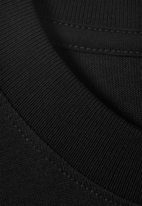 Sort bomuldsstof med ribstrikket rund hals og glat tekstur, kendetegnet ved pæn syning og en let glans. Nærbillede af stoflag.