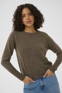Pull marron en tricot avec un col rond, des manches longues et des poignets côtelés, associé à un jean bleu clair. Texture douce et coupe décontractée.