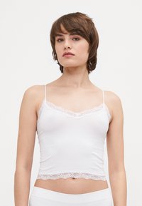 Witte camisole met kant langs de halslijn en zoom, voorzien van dunne verstelbare bandjes en een gladde stoftextuur.