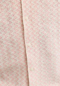 Gros plan d'un tissu tricoté avec un motif zigzag rose clair et blanc, et trois boutons blancs alignés verticalement.