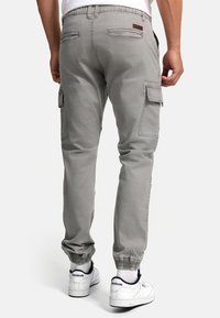 Graue Cargo-Hosen mit elastischen Bündchen, mehreren Taschen und einem Lederlabel auf der Rückseite. Kombiniert mit weißen Sneakers und einem lässigen T-Shirt.