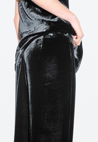 Black velvet pants with a soft texture, featuring a loose fit, wide legs, and a high waist, with a subtle sheen and draped detail.