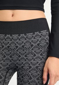 Leggings negros de cintura alta con un intrincado patrón de diamantes y corazones en gris, con una cinturilla texturizada y un acabado de tela suave.