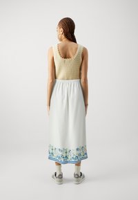 Strikket beige crop topp med bølgede kanter, sammen med en lys blå maxiskjørt med blomsterprint og blå stripet kant. Uformelle sko.
