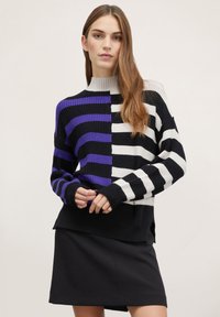 Maglione lavorato a maglia con strisce alternate nere, bianche e viola, con un colletto alto, texture a coste e maniche lunghe. Accoppiato con una gonna nera.