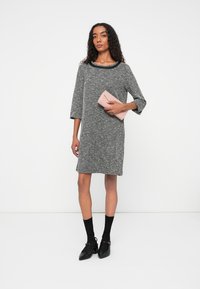 Rochie gri din țesătură tweed, cu mâneci trei sferturi, decolteu rotund și croială lejeră. Modelul ține în mână o poșetă roz. Pantofii și șosetele negre completează ținuta.