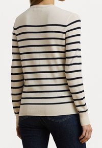 Pruhovaný svetr v barvách krémové a námořnické modři. Má dlouhé rukávy, kulatý výstřih a žebrovaný lem. Vzor zahrnuje horizontální pruhy po celém svetr.